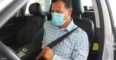 Conductor sentado dentro de un auto se coloca el cinturón de seguridad. Utiliza también un cubrebocas tricapa color celeste.